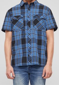 Chemise à manches courtes à carreaux bleus avec accents noirs et deux poches avant. Confectionnée en tissu doux, dotée d'une fermeture à boutons.