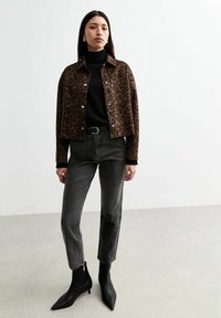 Leopardmönstrad kort jacka, svart polotröja, höga mörka jeans och svart spetsiga ankelboots med dragkedjor. Slät textur och figursydd design.