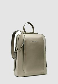 Sac à dos en cuir gris clair au design structuré, avec poignée supérieure, bretelles réglables et poches zippées. Présente un logo discret.