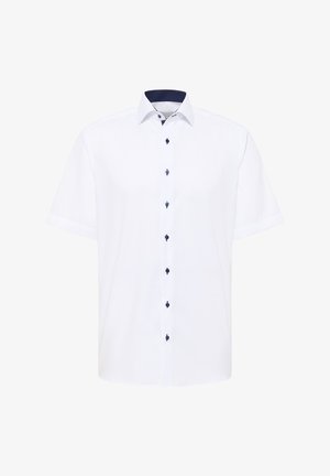 Chemise blanche à manches courtes avec un col, dotée de boutons bleu marine et d'un motif à pois bleu marine à l'intérieur du col.