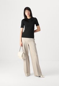 Maglietta nera aderente a maniche corte abbinata a pantaloni larghi beige chiaro. Tiene una borsa beige chiaro con tracolla a catena.