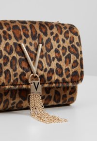 Leopardi-kuvioitu käsilaukku, jossa on kullanvärinen "V"-logo, teksturoitu turkismateriaali ja ketjuyksityiskohta suorakaiteen muotoisella "VALENTINO"-merkityllä koristeella.