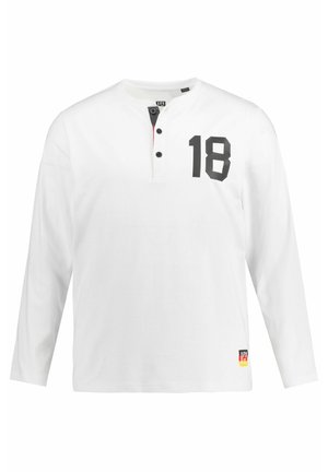 Wit overhemd met lange mouwen en zwarte knoopsluiting, met een groot zwart "18" op de voorkant en een klein merklabel aan de zoom.