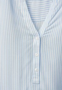 Devant de chemise à rayures verticales bleu clair et blanc, col en V avec trois boutons blancs le long de la patte centrale.