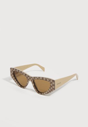 Brille med katteøyeform, brune tonede linser, beige stenger og en mønstret ramme med Gucci-logo; "GUCCI" trykt på stangen.