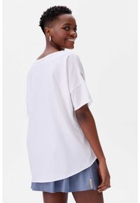 Witte oversized T-shirt, korte mouwen, relaxed fit, gebogen zoom. Gecombineerd met een lichtblauwe geplooide rok met een klein label.