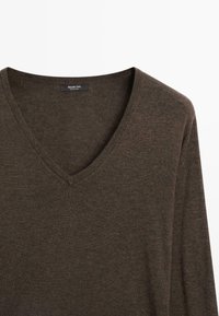 Pull marron à manches longues et col en V en tissu tricoté fin avec une étiquette de marque visible à l'intérieur du col.