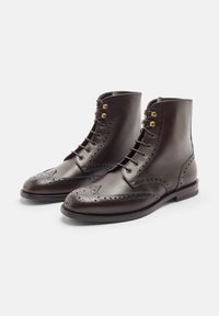 Stivaletti alla caviglia in pelle marrone con dettagli brogue, punta rotonda e occhielli in ottone. Texture liscia con design con lacci e tacco basso.