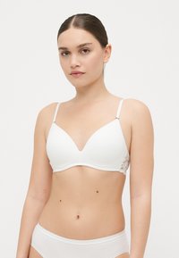 Soutien-gorge blanc avec un décolleté plongeant, tissu lisse et accents en dentelle sur les côtés. Bretelles réglables et design sans couture.