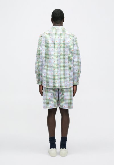 Σετ πουκάμισο και σορτς με πράσινο και λευκό καρό σχέδιο, με χαλαρή εφαρμογή και ελαφρύ ύφασμα. Λευκά αθλητικά παπούτσια και σκούρες μπλε κάλτσες.