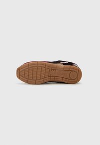 Sneaker nera con un accento viola, caratterizzata da una suola testurizzata, suola in gomma e un motivo a rete per la trazione. Dettaglio del tallone con marchio visibile.