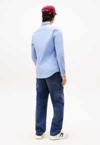 Lys blå langermet skjorte med kneppede mansjetter, brukt sammen med mørkeblå, løstsittende cargobukser og hvite joggesko med røde og blå detaljer.