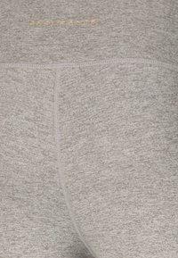 Gros plan sur un tissu texturé gris clair avec des détails de couture et le mot « ENDURANCE » brodé en petites lettres capitales dorées près du haut.