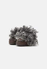 Brūni zamšādas čības ar curly pelēku un balto mākslīgo kažokādu augšējā daļā, ar noapaļotu formu un šūtām detaļām gar malām.