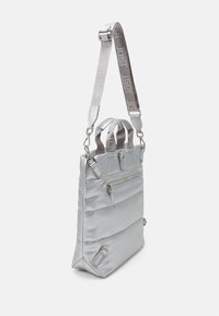 Stříbrná polstrovaná taška s dvěma horními uchy a nastavitelným popruhem. Obsahuje přední zipovou kapsu a hardware ve stříbrném odstínu. Hladká textura.