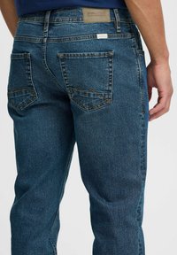 Jeans de mezclilla azul con corte recto, que cuentan con dos bolsillos traseros con un patrón de costura en zigzag y una etiqueta en la cintura.