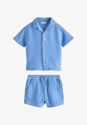 Småbarn iført lyseblå tekstureret kortærmet skjorte med knapper og matchende shorts samt brune sandaler med spænde på en lys baggrund.