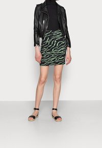 Chaqueta de cuero negra sobre un cuello de tortuga negro, combinada con una mini falda a rayas verdes y negras y sandalias de espadrille negras con tiras al tobillo.