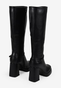 Stivali neri al ginocchio realizzati in pelle liscia. Presentano un tacco quadrato, una cerniera laterale e un accento a cinturino vicino alla caviglia.
