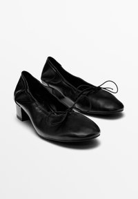 Ballerine in pelle nera con punta affusolata, fiocco decorativo e tacco basso e spesso. Texture liscia e design minimalista.