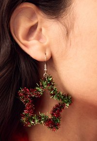 Red and green star-shaped earrings made of tinsel, hanging on a silver hoop, with a shiny and textured finish.