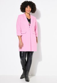 Blazer rosa con mangas de tres cuartos, dos bolsillos frontales y un solo botón. Combinado con leggings negros ajustados y botas de tobillo con tachuelas.