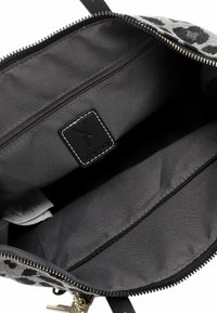 Atvērta melna un pelēka plecu soma, kas parāda plašu interjeru ar rāvējslēdzēja kabatu un iešūtu zīmola etiķeti iekšpusē.