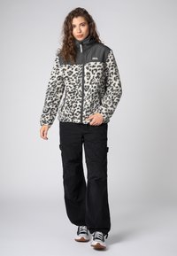 Fleece jacket with leopard print, gray upper, full zip, high collar. Black cargo pants, casual sneakers with white and brown accents.