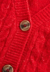 Cardigan rosso lavorato a maglia con un motivo a treccia, tessuto testurizzato e un grande bottone marrone con accenti rossi.