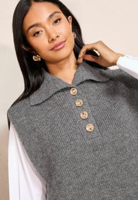 Hallide kootud vest, millel on krae ja neli suurt kreemivärvi nuppu. Tekstureeritud kangas ribakujundusega.