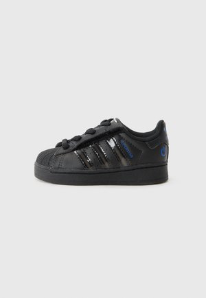 Baskets Adidas Superstar noires avec lacets noirs, trois bandes brillantes et accents bleus sur un fond gris clair.