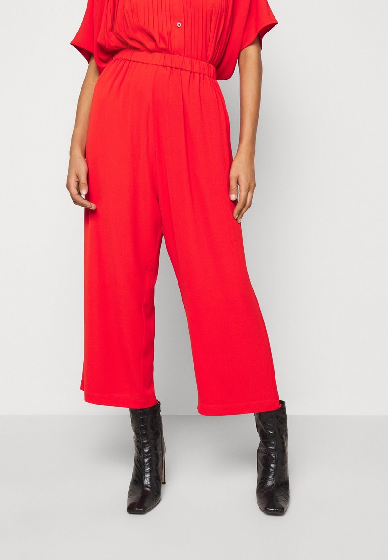 Pantalones rojos de pierna ancha con cintura elástica, tejido fluido y una textura suave, combinados con botas de tacón alto negras.
