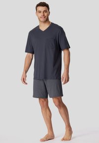 Dunkelgraues V-Shirt mit einem Brusttasche, kombiniert mit gemusterten Shorts, die kleine weiße Punkte auf einem Marinehintergrund zeigen.
