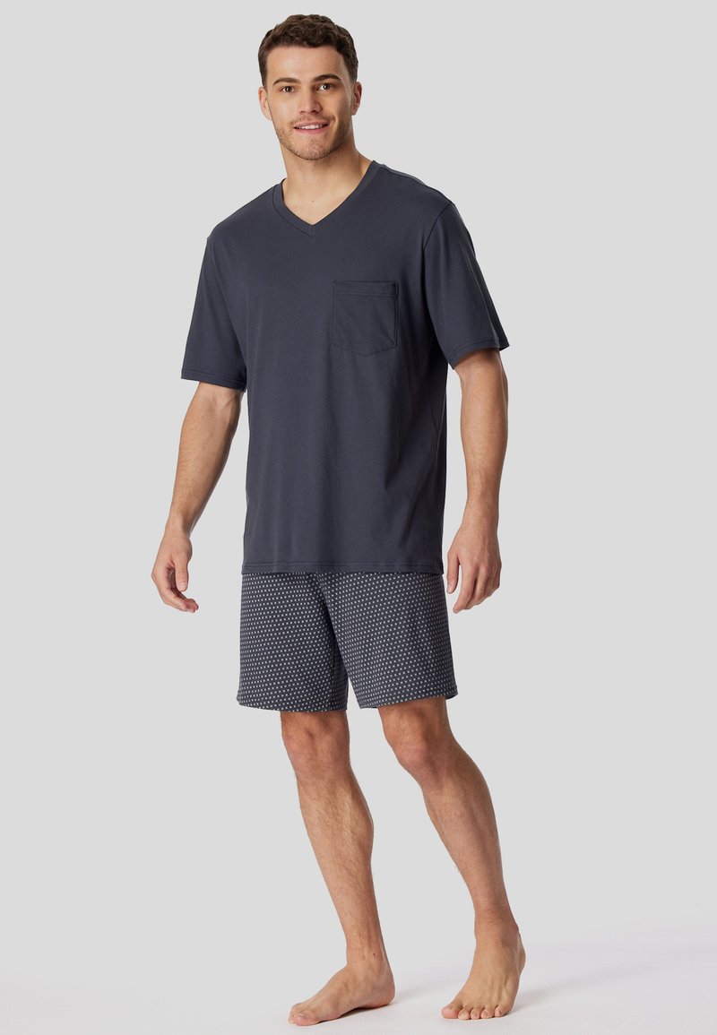 Dunkelgraues V-Shirt mit einem Brusttasche, kombiniert mit gemusterten Shorts, die kleine weiße Punkte auf einem Marinehintergrund zeigen.