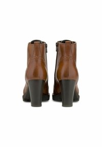 Hnědé kožené kotníkové boty s hladkým povrchem, vybavené bočním zipem a pevnými blokovými podpatky. Dekorativní prošívání podél švů.
