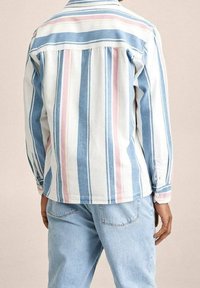 Biała koszula zapinana na guziki w niebieskie i różowe pionowe paski, z długimi rękawami i yoke na plecach, zestawiona z jasnoniebieskimi dżinsami.