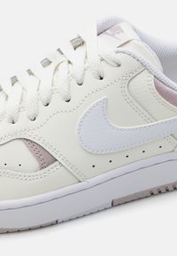 Bijele kožne tenisice s svijetloružičastim naglascima, teksturiranim swoosh logotipom, ravnim bijelim vezicama i gumenim potplatom s malim utorima.