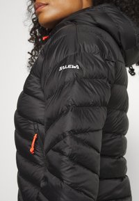 Black puffer jacket with chevron quilting, featuring a hood and orange zipper pull, branded with white "SALEWA" logo on the shoulder.