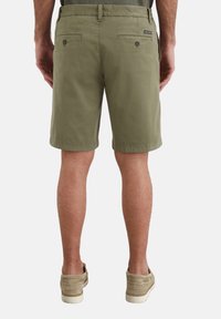 Shorts en chino vert olive en coton, dotés de deux poches arrière avec boutons, coupe droite et ourlet roulé. Portés avec des chaussures slip-on beige.