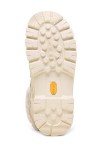 Valkoinen kumipohja, jossa on teksturoitu pito, varustettuna pyöreillä napeilla ja keskellä keltaisella Vibram-logolla.