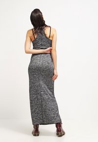 Dlouhá šedá maxi šaty s texturovaným, melírovaným vzorem a tenkými ramínky. Nosené s burgundskými kotníkovými botami, zobrazené ze zadu.