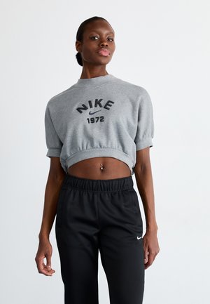 Pilkas trumpas megztinis su "NIKE 1972" spauda, trumpomis rankovėmis; derinamas su juodomis kelnėmis su elastinga juostele, kurių gale yra mažas baltas logotipas.