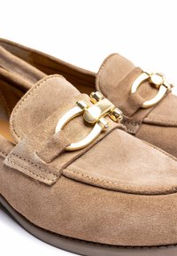 Beige suède loafers met een ronde neus, een opvallende gouden hardware-accent en gestikte details langs de randen. Glad textuur.