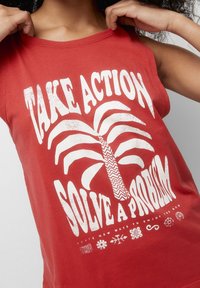 Rød tanktop med et hvidt grafisk design af et palmetræ med teksten "TAG HANDLING LØS ET PROBLEM" og forskellige dekorative symboler.