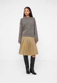 Gray knit sweater with ribbed hem, beige pleated skirt, and knee-high black leather boots, showcasing a textured, layered look.