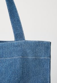 Denim maišelį, pagamintą iš tvirto mėlyno audinio, pasižymintį švariu dizainu, tiesiais viršutiniais kraštais ir kontrastingomis baltomis siūlėmis.