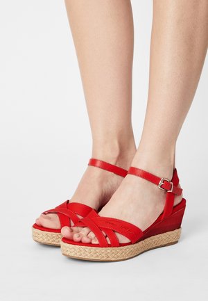 Sandales compensées rouges avec une semelle intermédiaire en jute tressé, dotées de brides croisées et d'une boucle à la cheville pour un ajustement réglable. Tige en synthétique lisse.