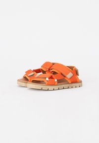 Orange tygsandaler med justerbara kardborreband, texturerade innersulor och tanfärgade gummisulor med en mönstrad sula.