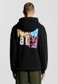 Juodas džemperis su gausiai marginta raidžių ir raštų koliažo kompozicija ant nugaros, turintis laisvą siluetą ir gobtuvą su raišteliais.