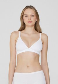 Bralette blanco con forma triangular, tirantes finos ajustables y textura de algodón suave. Diseño sencillo sin herrajes visibles ni patrones.